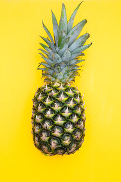 A tropical pineapple fruit on a yellow background. Vertical photo