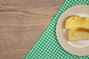 Freshly baked homemade cake slices and green checkered tablecloth on wooden table. Top view with copy space.