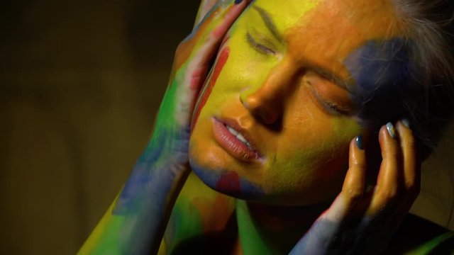 Tired woman in multi-colored bodyart stands with her eyes closed
