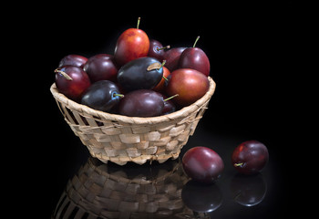 Juicy fresh plum in a basket on glass. On a black background