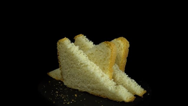 Close-up of sliced white wheat bread rotates against a black background, loopy motion.