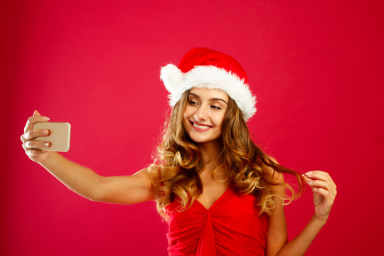 Young happy Santa woman in red dress taking her selfie over red background