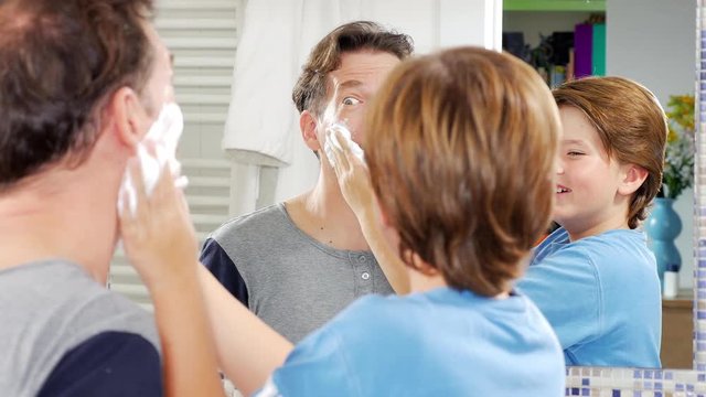 Father letting son putting shaving cream on his face funny closeup