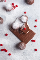 chocolate round candies, chocolate bars and red berries on a gray background and powdered sugar