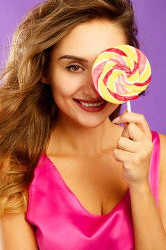 Portrait of a happy pretty girl holding sweet candy over violet background