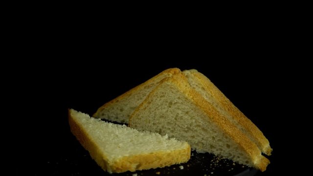 Close-up of sliced white wheat bread rotates against a black background, loopy motion.