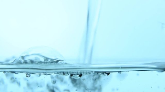 Pouring pure clear cold water in transparent glass jar or teapot until full, close up, low angle side view, slow motion