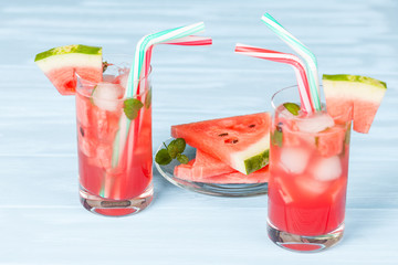 Watermelon lemonade with ice and mint leaves. Homemade lemonade of ripe berry with red and green ripes. Glass of cold watermelon tea. Refreshing summer drink. Cocktail on a wooden background