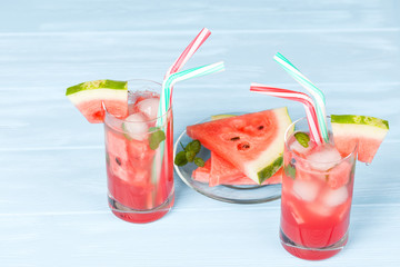 Watermelon lemonade with ice and mint leaves. Homemade lemonade of ripe berry with red and green ripes. Glass of cold watermelon tea. Refreshing summer drink. Cocktail on a wooden background