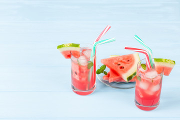 Watermelon lemonade with ice and mint leaves. Homemade lemonade of ripe berry with red and green ripes. Glass of cold watermelon tea. Refreshing summer drink. Cocktail on a wooden background