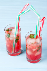 Watermelon lemonade with ice and mint leaves. Homemade lemonade of ripe berry with red and green ripes. Glass of cold watermelon tea. Refreshing summer drink. Cocktail on a wooden background