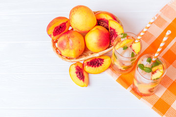 Peach lemonade with ice and mint leaves. Homemade lemonade of ripe nectarine with white and orange ripe. Two glasses of peach tea. Refreshing summer drink on a white wooden background.