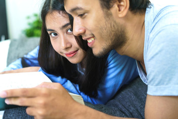 Young asian lover lying on the bed reading book in bedroom. concept of education, tutorial and...