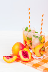 Peach lemonade with ice and mint leaves. Homemade lemonade of ripe nectarine with white and orange ripe. Two glasses of peach tea. Refreshing summer drink on a white wooden background.