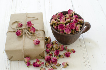 Cup with dry roses and gift box on a wooden background