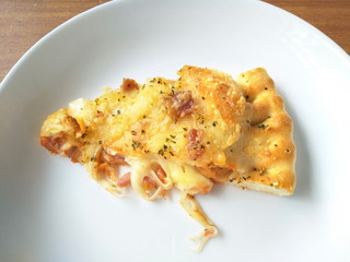 piece of  ham, bacon and cheese puff pizza on white plate on wood table