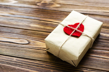 gift box wrapped in kraft paper and red wooden heart on wooden table
