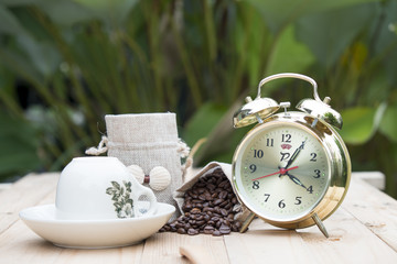 Bag of coffee beans and a cup of coffee on the table with cup and clock