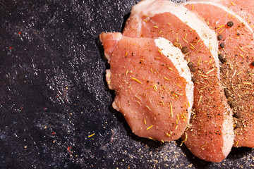 Top close up view on uncooked meat seasoned with spices, pepper and salt on dark wooden board