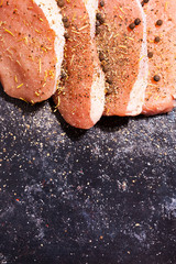 Top close up view on uncooked meat seasoned with spices, pepper and salt on dark wooden board