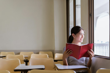 Asian beautiful young woman reading red book and sit side window. concept of education, learning, knowledge, information and big data.