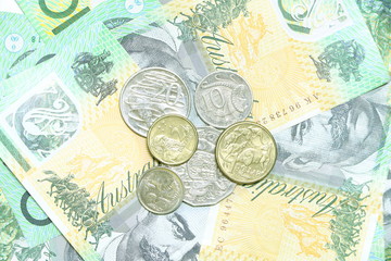 Many coins of Australian money on group of 100 dollar Australian notes pile background