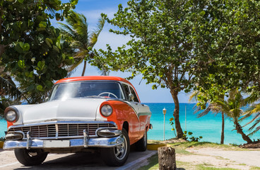 Amerikanischer orange weisser Ford Fairlane Oldtimer parkt direkt am Strand unter Palmen in...