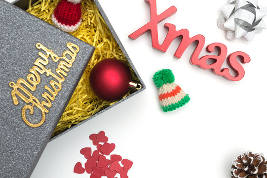 Merry christmas and X-mas text, fur hat, ball, ribbon, pine cone, heart in black gift box with yellow packaging material