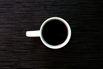 White cup of coffee on black background. White ceramic cup with black coffee.