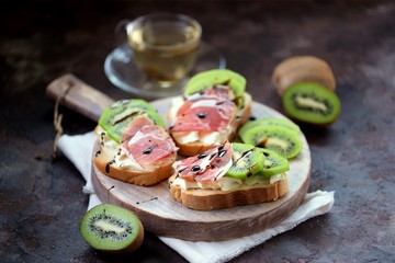 Fototapeta na wymiar Sandwiches with soft cheese, Parma ham, kiwi and balsamic cream. Healthy breakfast.