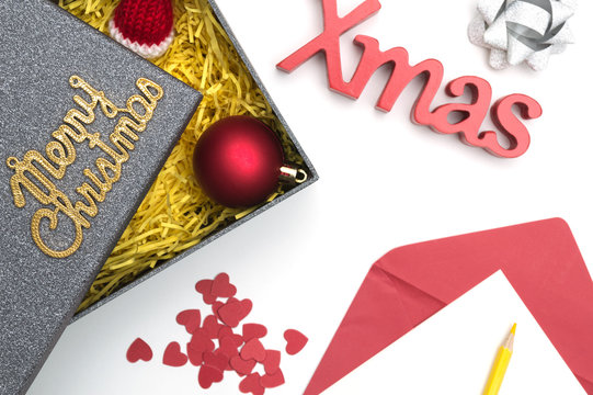 Merry christmas and X-mas text, fur hat, ball, ribbon, christmas card, color pencil, heart in black gift box with yellow packaging material