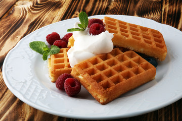 Plate of belgian waffles with whipped cream, mint and fresh berries