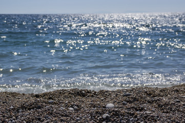 Pebble beach with blue sea and waves with sun reflections