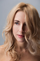 Naklejka premium Serious middle-aged woman with blond hair is standing with naked shoulders and looking aside pensively. Isolated background