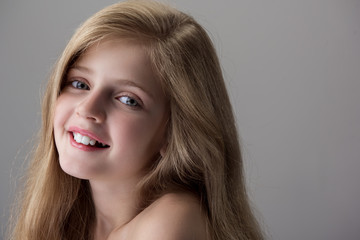 Feeling glee. Close-up of face of happy adorable little girl with naked shoulders is standing and looking at camera with joy. Isolated background with copy space in the right side