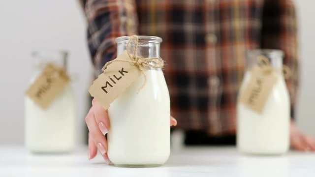 Woman moves one of three glass bottle towards camera offering milk. Quality dairy products. Healthy lifestyle. Calcium and vitamin D. Slow motion