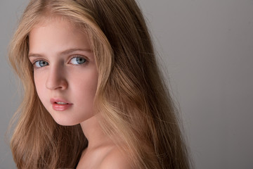 Fototapeta premium Close-up of face of pretty child with naked shoulders and long hair is standing and looking at camera dreamily. Isolated background