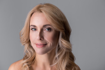 Fototapeta premium Close-up portrait of gorgeous middle-aged naked woman. She is looking at camera thoughtfully. Isolated background