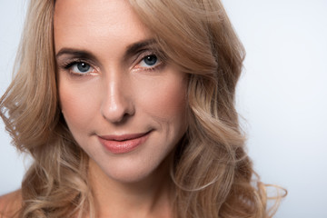 Naklejka premium Close-up portrait of gorgeous charming middle-aged woman with fresh skin and long hair. She is looking at camera with slight smile. Isolated background
