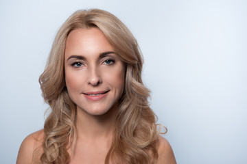 Fototapeta premium Elegant beauty. Portrait of charming middle-aged naked woman is looking at camera with joy. Isolated background. Copy space