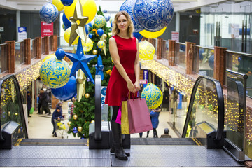 Obraz premium Young beautiful girl enjoys shopping in a shopping center with bright packages on the background of a Christmas tree