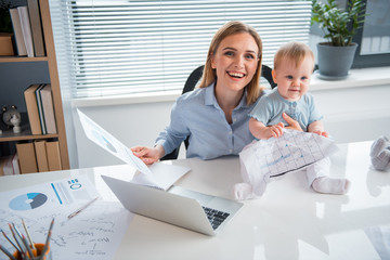 Top view cheerful mother having job at desk and taking care of baby in room. Profession and infant...