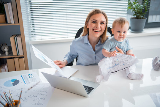 Top view cheerful mother having job at desk and taking care of baby in room. Profession and infant concept