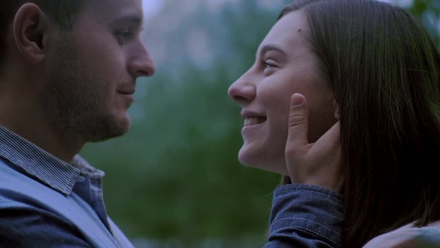 a guy and a girl look into each other's eyes. the guy is holding the girl's hands behind his face. Close up