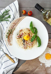 beautiful serving traditional Italian carbonara with egg yolk with a bottle of wine on a gray wooden background