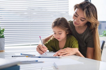 Obraz premium Portrait of friendly family drawing on paper with joy. Mother is embracing girl with love while they holding pencil together. Copy space