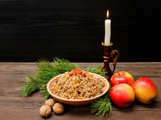 Dish of traditional Slavic treat on Christmas Eve.  Pine branches, candles, apples, walnuts. Brown and blak wooden background. Copy space