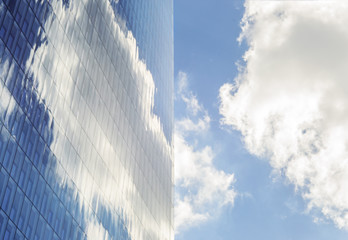 Sky and clouds reflected in windows of modern  tall office building. Skyscraper on background of blue sky with clouds. Simmetry and lines.