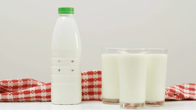 Woman puts a bottle on the surface where three glasses of fresh milk stand. Healthy lifestyle