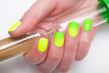 Woman with green and yellow manicured nails holding a hourglass
